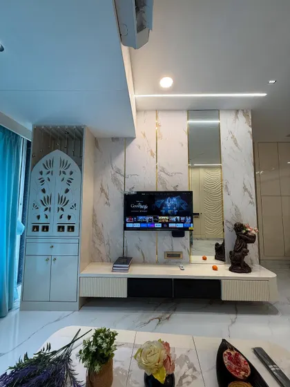 A glimpse of a finished living room in Mumbai, integrating a custom TV unit with marble-finish panels and a beautifully crafted pooja mandir with jaali work. The design balances modern aesthetics with traditional values.