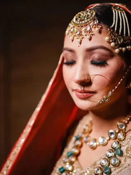 A serene, close-up bridal portrait. With her eyes closed, the focus is on her stunning makeup, the intricate details of her maang tikka, and her peaceful expression.