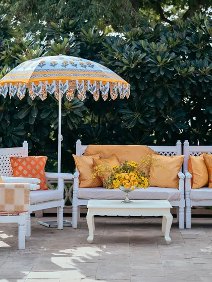A comfortable lounge setup with yellow and orange cushions, set against a backdrop of lush greenery.