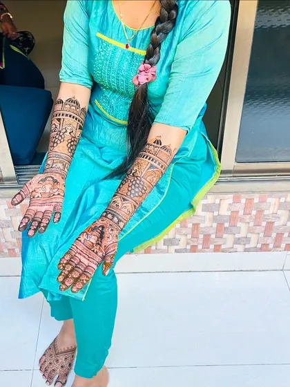A full view of a happy client with her engagement henna on both arms and feet. The design is consistent and flows beautifully from hands to feet.