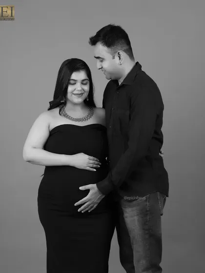 A simple and elegant black and white couple's portrait. The focus is on their hands gently placed on the baby bump.