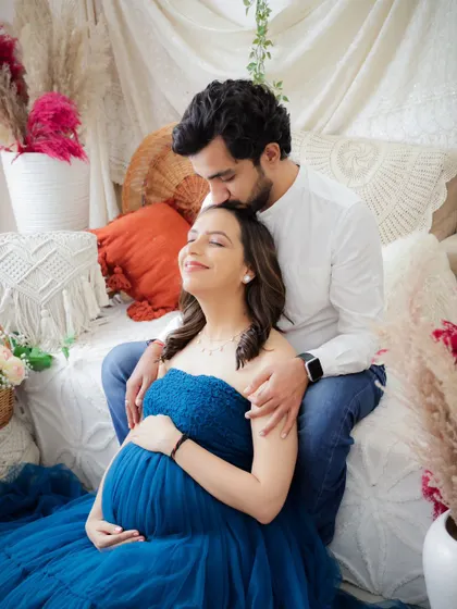 A serene and loving couple's portrait. The dad-to-be gently kisses his partner's forehead as she cradles her bump, surrounded by a beautiful blue gown.