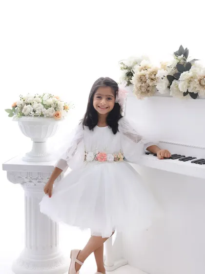 A fairytale portrait of a little girl in a beautiful white dress, standing by a miniature white piano. This setup is perfect for capturing a child's magical imagination.
