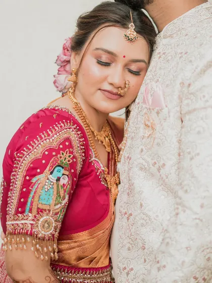 A close-up showcasing the intricate details of the bridal blouse, featuring a painted depiction of Radha and Krishna. The makeup is kept soft to complement the artistry of the outfit.