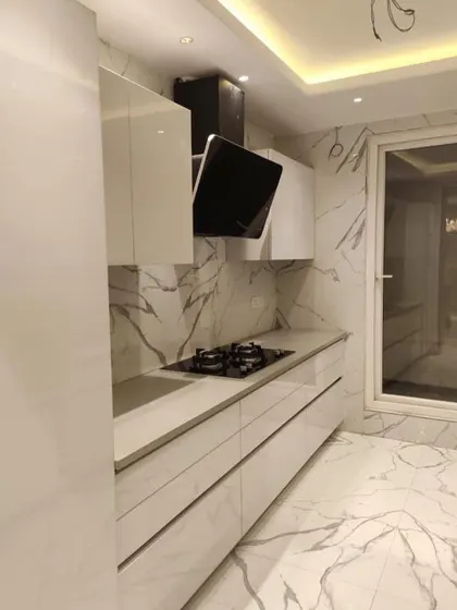 Another view of the all-marble look parallel kitchen, focusing on the cooking area with its sleek hob and chimney. The handleless design ensures an uninterrupted, clean look.