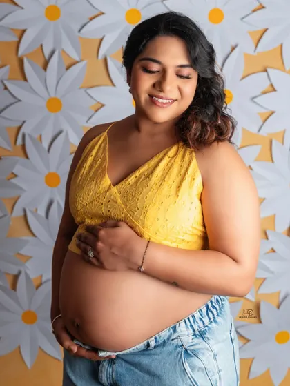 A sweet and sunny portrait against a wall of daisies. This mom-to-be's smile perfectly matches the cheerful and bright atmosphere of the photo.