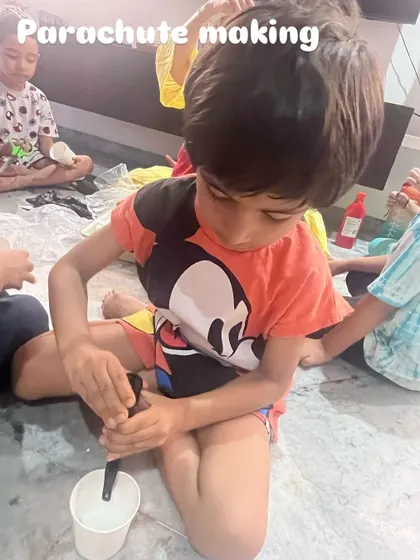 A child is carefully constructing his own parachute. This activity was part of our STEAM session on gravity, where we explored Isaac Newton's famous apple and why objects fall at different speeds.