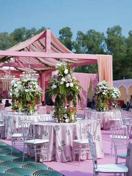 An overview of the outdoor lunch setup. The pink mandap structure, custom tablecloths, and lush floral centerpieces create a cohesive and beautifully romantic dining experience for guests.