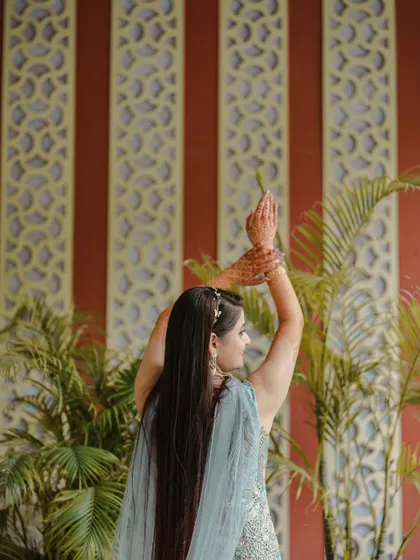 An artistic shot of the bride, focusing on her graceful posture and the details of her Mehendi. The architectural background adds a touch of elegance.