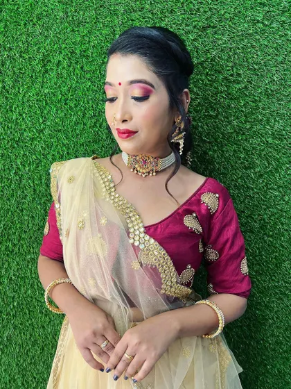 A portrait of the client in her festive cream and maroon lehenga. The makeup features a subtle red eyeshadow and matching lip, creating a cohesive and elegant look for a wedding guest.