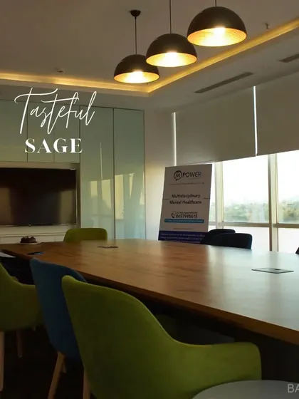 A tasteful and sage conference room. The large wood table is surrounded by chairs in muted green and blue tones, creating a professional yet stylish meeting space.