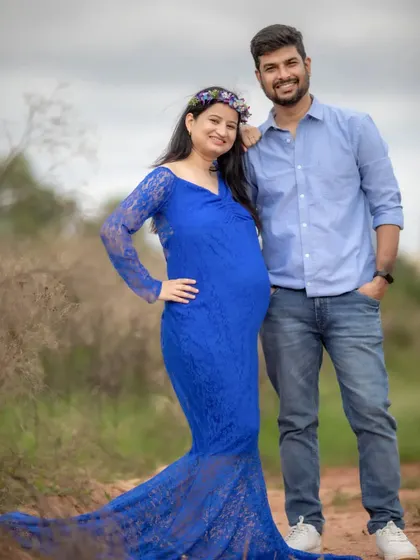 A beautiful outdoor portrait of an expecting couple. The mom-to-be looks stunning in a blue lace gown, complemented by a flower crown, creating a romantic, fairytale look.