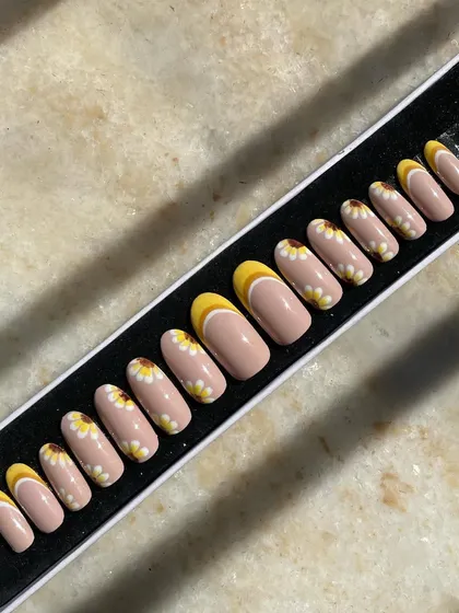 Sunflowers and sunshine to brighten your day. This custom set features hand-painted daisies and a cheerful yellow French tip design on a nude base. It's a happy, floral design perfect for any season.