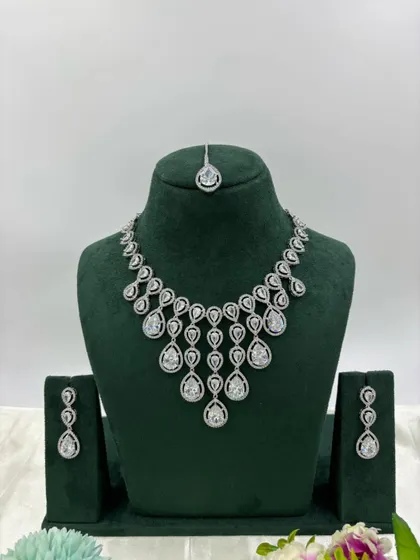 An elegant AD necklace set with a matching maang tikka. The cascading design with teardrop stones is available in green, pink, and all-white, perfect for receptions and parties.