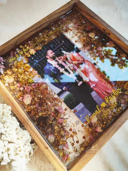 A 12x12 inch teakwood frame preserving a couple's varmala. The flowers are arranged to create a soft, romantic border around their photo.
