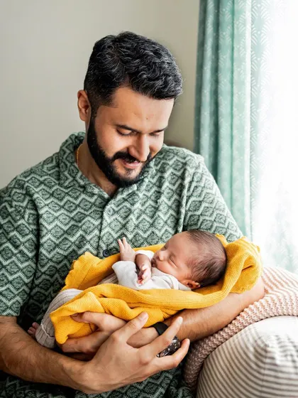A proud father holding his newborn by the window. The natural light highlights the tender connection between them in this lifestyle shot.