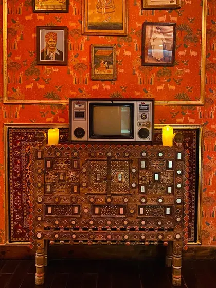 A symphony of cultures. This corner features a vintage television set atop an intricately carved chest, set against a backdrop of royal portraits and carpets.