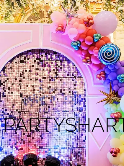A shimmering sequin backdrop panel for a candy-themed party, adorned with colorful balloon clusters and a lollipop prop.