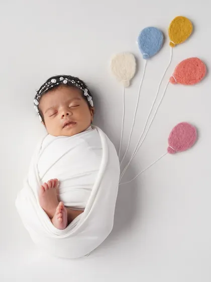 So simple, yet so sweet. This little one is wrapped snugly and holding onto tiny felt balloons, creating a whimsical and adorable image.