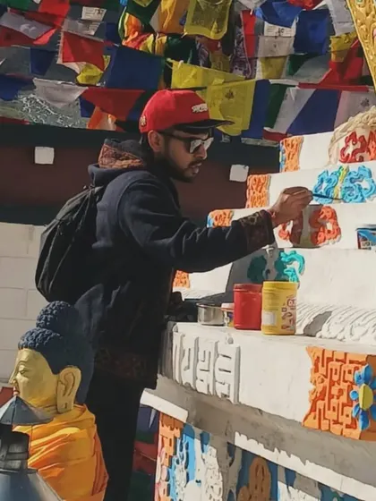 A closer look at the detail work. I am carefully applying paint to the intricate patterns on the base of the Stupa, fully focused on the task at hand in this high-altitude environment.