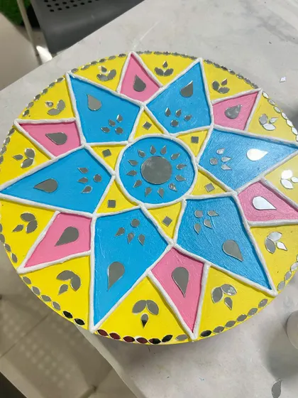 A geometric star-patterned mirror art piece in bright yellow, pink, and blue.