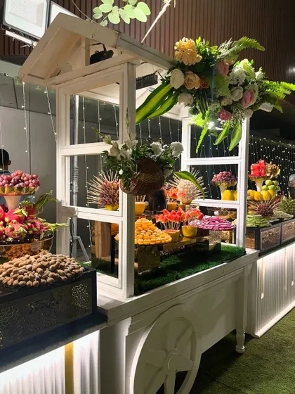 An elaborate fruit display centered around a charming white cart, adorned with fresh flowers.