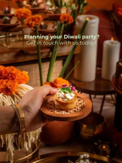 A close-up of a guest holding one of our savory tartlets. The background shows a festive Diwali setup with marigolds and candles, and the text overlay serves as a direct call to action for party planning.