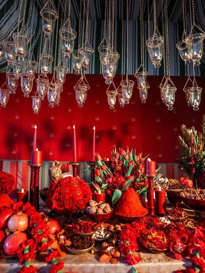 An 'Ode to India' tablescape featuring a maximalist aesthetic with a mountain of red flowers, spices, and fruits, set under hanging glass lanterns.