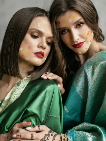 The colors of Holi representing a bond of love and friendship. Two models in matching sarees share a moment of quiet connection, their faces touched with festive colors.