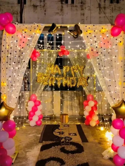 A terrace decoration with a fairy light curtain, "Happy Birthday" banner, and pink and white balloon columns.