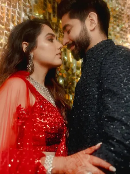 An intimate close-up of the couple against a shimmering gold backdrop. The warm lighting and their close embrace capture the romance of the Sangeet night.
