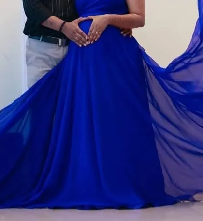 A close-up of a couple's hands forming a heart on the baby bump, with the blue gown creating a beautiful frame.