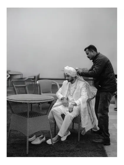 A behind-the-scenes black and white shot of the groom having his turban tied. This candid moment captures the preparation and tradition involved in getting ready.