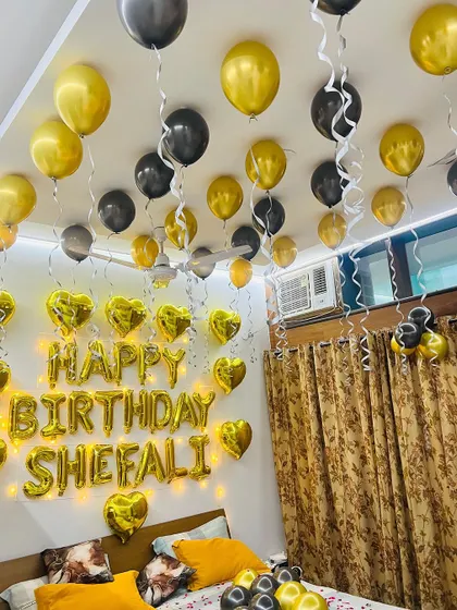 A birthday room decoration for Shefali with gold 'Happy Birthday' foil letters surrounded by heart-shaped foil balloons and fairy lights.