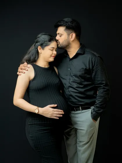 A tender moment captured against a simple black background. The partner's gentle kiss on the forehead and the mother's peaceful expression make this a very emotional portrait.