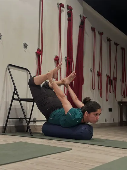 This is a supported variation of Dhanurasana (Bow Pose). The bolster supports the abdomen while the chair provides stability, allowing the spine to awaken and open safely. This is how we make advanced poses therapeutic and accessible.
