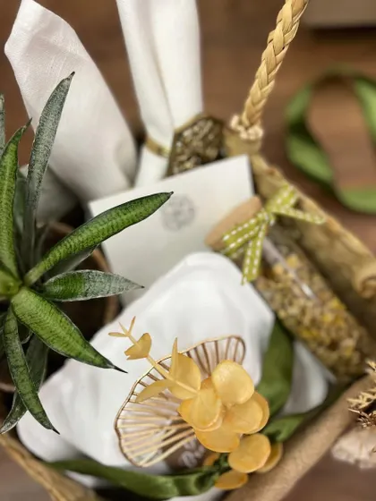 A luxury hamper focused on sustainable and natural elements. It features a live snake plant, linen napkins with artisanal rings, and a vial of herbal tea, all arranged in a rustic basket.