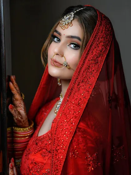 A classic bridal portrait in a stunning red lehenga. The bride looks directly at the camera with a gentle confidence, her beauty enhanced by the soft lighting and traditional attire.