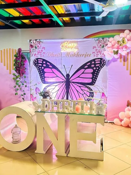 A beautiful butterfly themed first birthday party with a large butterfly backdrop, "ONE" table, and pink and green balloon decorations.