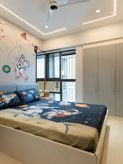 A full view of the space-themed bedroom, showing the neutral gray wardrobe and simple bed frame that balance the playful wallpaper and linens.