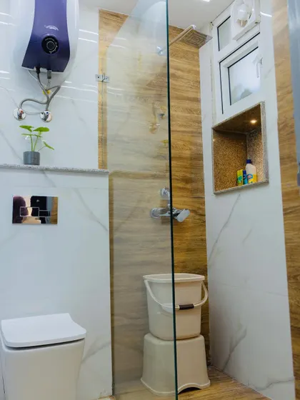 This bathroom uses a combination of white marble and wood-finish tiles to create a warm and inviting space. A glass partition separates the wet and dry areas, and a niche in the wall provides storage.