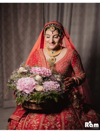 A sweet portrait of the bride holding a basket of flowers, her gentle smile and beautiful red lehenga creating a picture of classic bridal elegance.