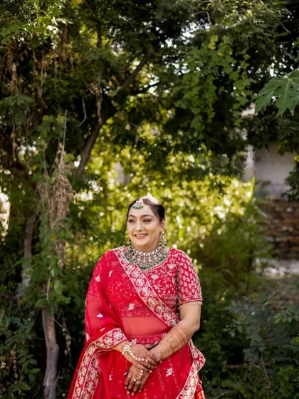A full length portrait of the bride in a beautiful garden setting. The vibrant red of her lehenga stands out, and her makeup is perfectly balanced for an outdoor ceremony.
