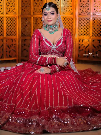 A full-length shot of a bride seated in a vibrant red lehenga with silver gota patti work. The pose is regal and showcases the entire expanse of the beautiful skirt.