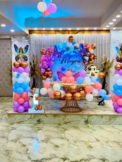 A wide view of the butterfly-themed stage decoration in a banquet hall. The setup includes a cake table, balloon pillars, and a custom backdrop, all coordinated in beautiful pastel colors.