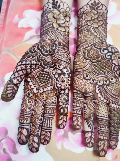 The palms are decorated with a dense network of traditional motifs, including paisleys, dots, and fine lines.