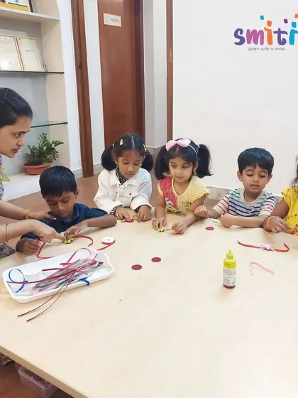 A group of children at a table, each engrossed in making a special Rakhi. The classroom buzzes with creative energy during our festival preparations.