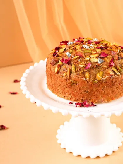 A side profile of the Mawa cake, highlighting its texture and height against a warm, soft-focus background.