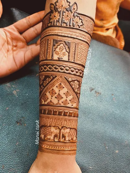 A beautiful example of Indian bridal mehendi extending up the forearm. The design is divided into sections with different patterns, including elephants, architectural jharokhas, and floral motifs.