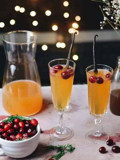 A festive cranberry and vanilla bean cocktail. The bokeh lights and holiday-themed props immediately set a celebratory Christmas mood, perfect for seasonal drink menus.